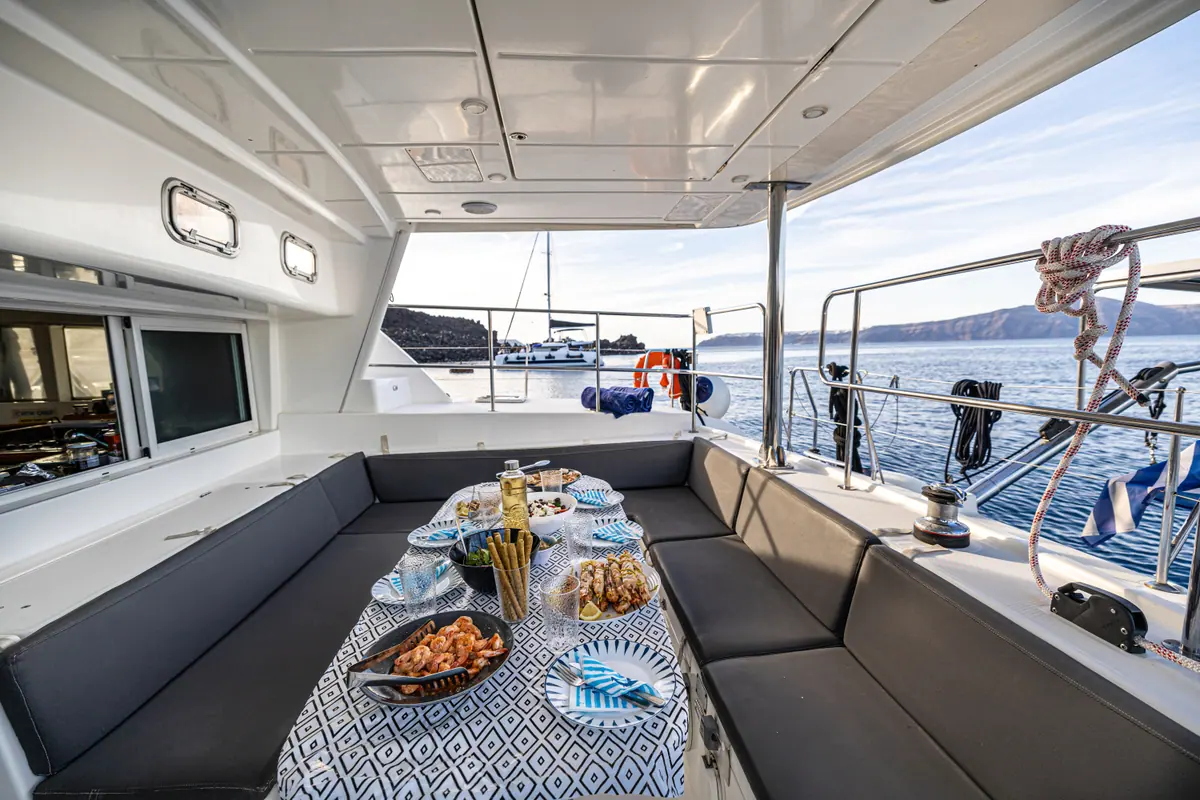 The cockpit table laid for lunch — bread, cheese, olives and skewers — with the sea past the rail.